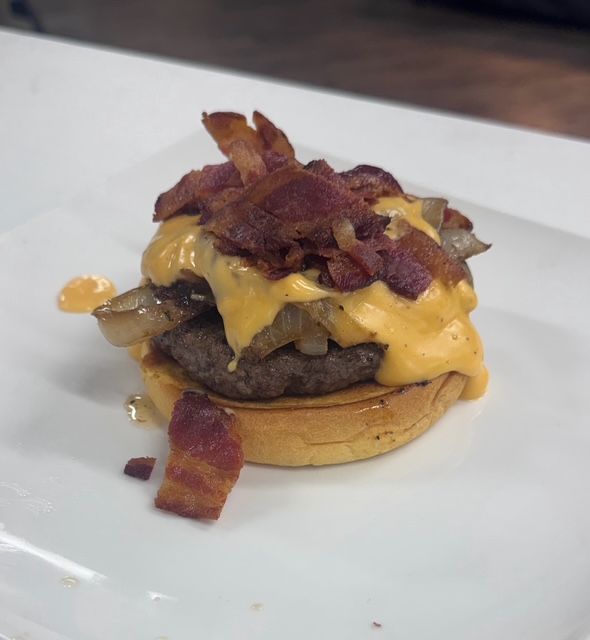 A burger topped with melted beer cheese and strips of bacon on a toasted bun.