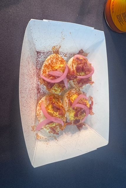 Deviled eggs garnished with pickled red onion, served in a paper boat.