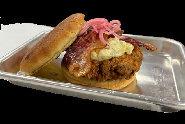 A popper chicken sandwich topped with pickled red onion, served on a metal tray.