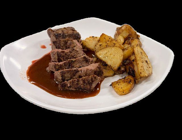Sliced prime sirloin with roasted potatoes and pan sauce on a white plate.