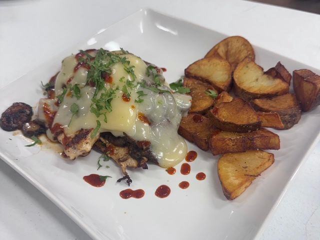Smothered chicken topped with melted cheese and herbs, served with roasted potatoes.