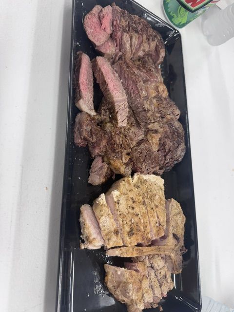 Sliced steak and grilled chicken arranged together on a dark serving tray.